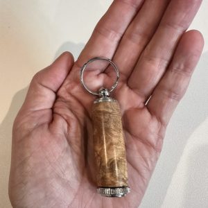 Hand-turned maple burl pill holder keychain shown in hand for scale