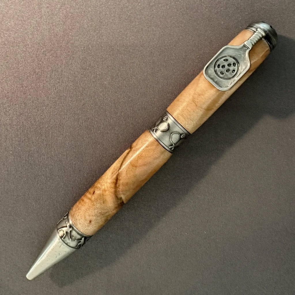 Maple pickleball pen with antique pewter hardware and a paddle-shaped clip, displayed diagonally on gray fabric.