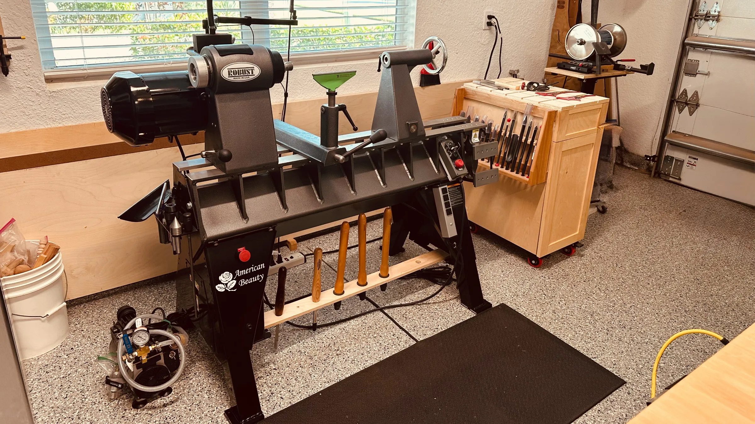 Robust American Beauty lathe with task lights, a tool cabinet, and a sharpening station nearby.
