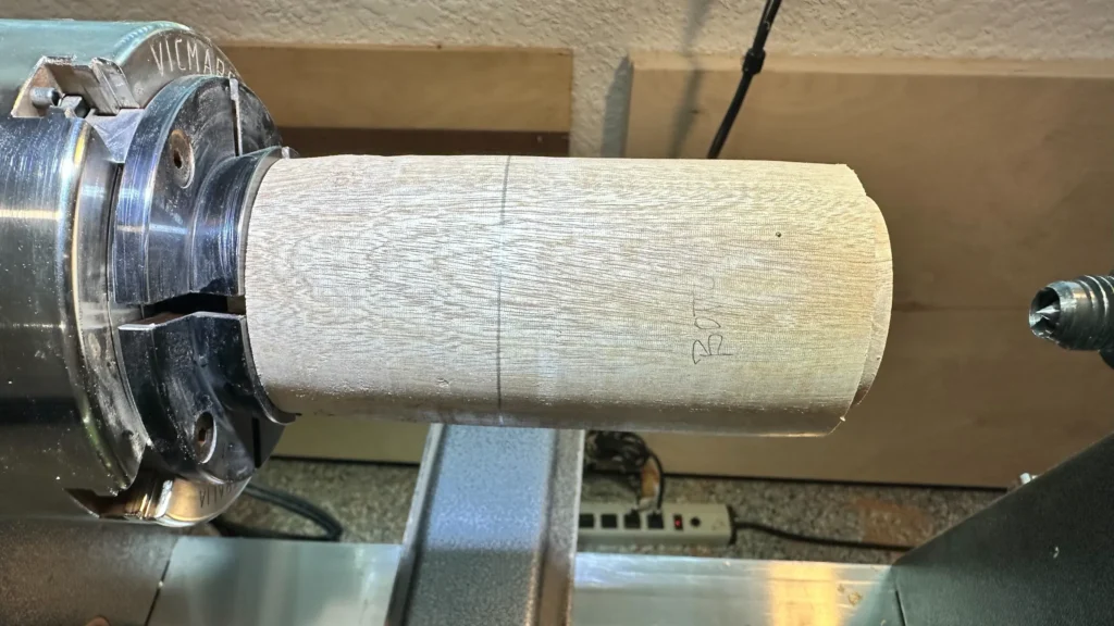 Cylindrical Sipo mahogany blank held in the lathe chuck with pencil lines marking the planned divisions.