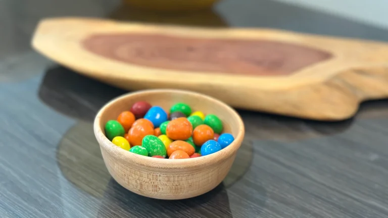 Wooden bowl filled with colorful candy on a side table, with a live-edge wooden display riser behind it.