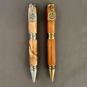 Two wooden pickleball pens with paddle clips, shown in antique pewter and antique brass finishes.
