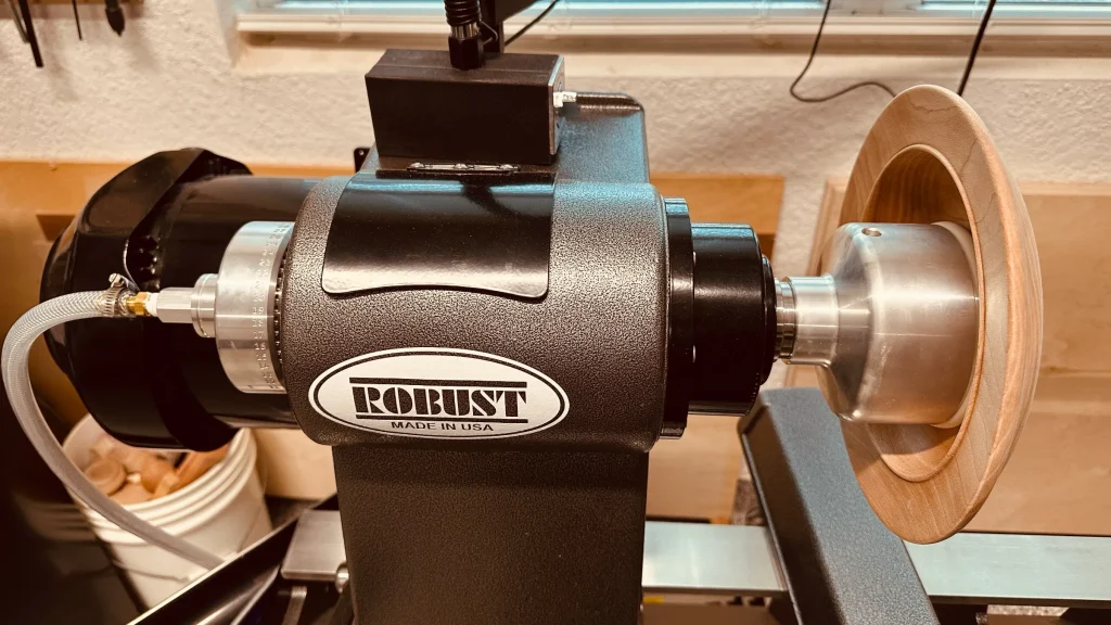 Aluminum vacuum chuck holding a wooden piece from inside on a Robust lathe, with the vacuum hose connected behind the headstock.