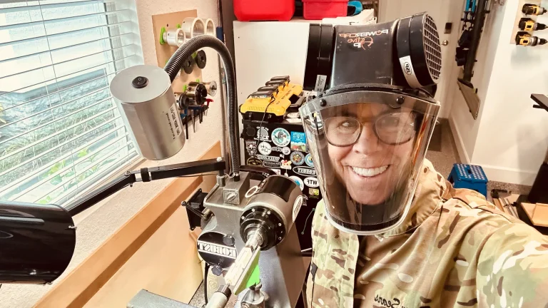 Rogene Sears smiling beside her lathe while wearing a Powercap Active IP face shield and protective eyewear.