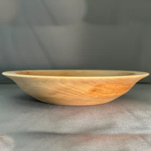 Side view of a shallow sycamore wood bowl with a thin rim, gently curved base, and warm golden grain.