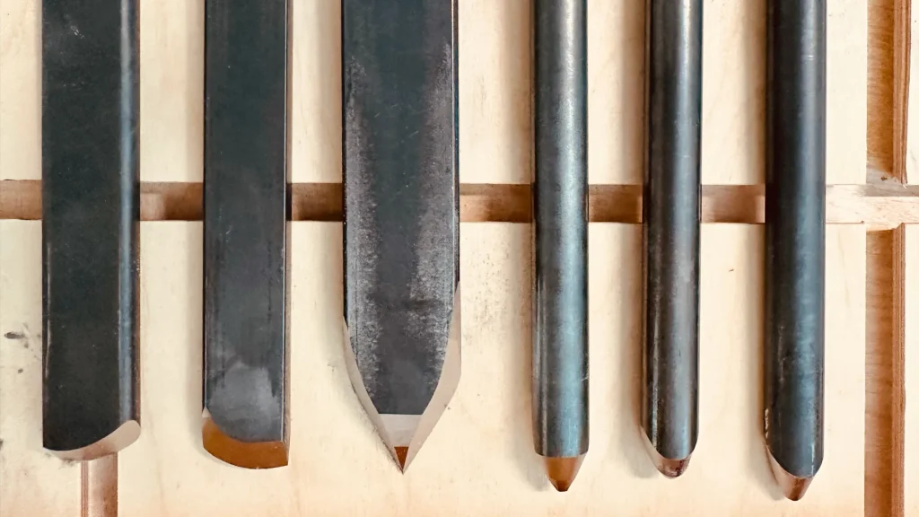 Close-up of six traditional woodturning tools showing their different cutting profiles on a wooden surface.