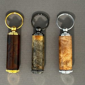 Three hand-turned wooden pill holder keychains arranged side by side with gold, dark, and silver-colored hardware.